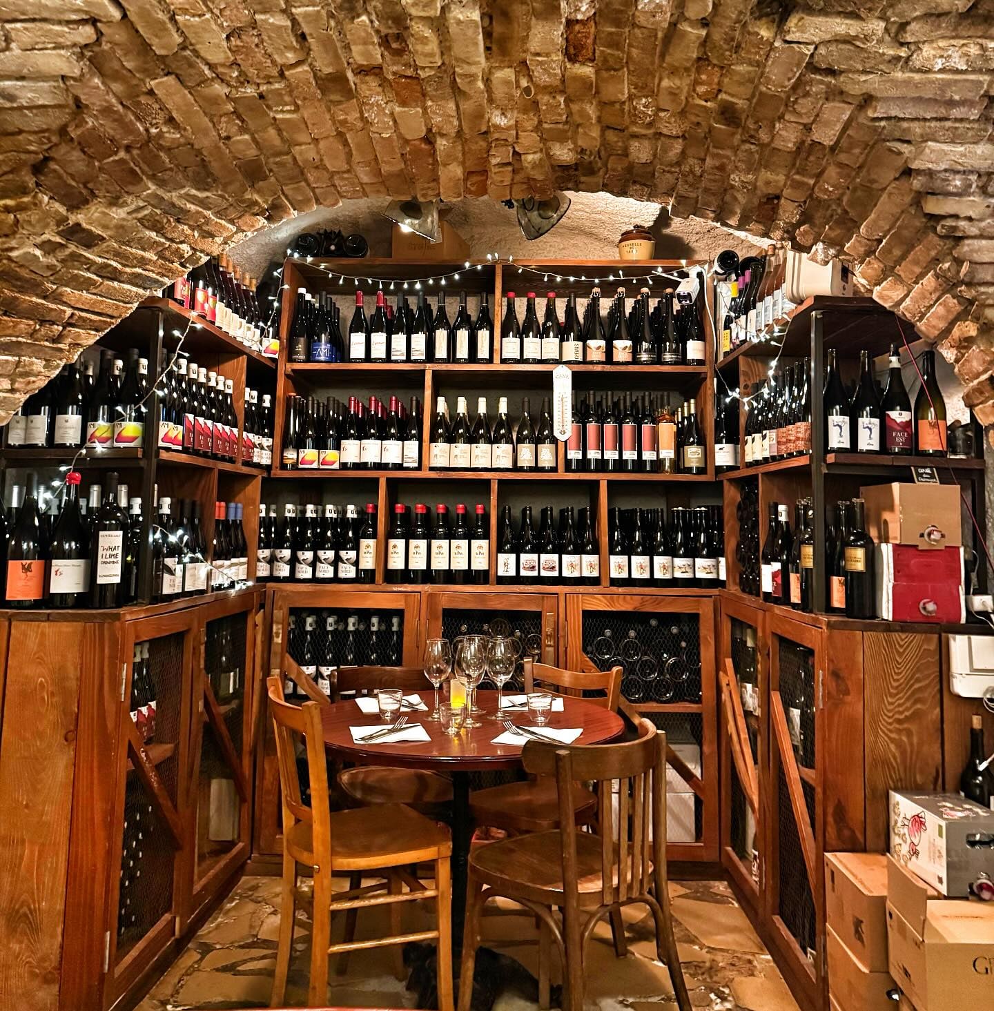 Voûte en briques de la cave à vins, table ronde dressée pour quatre sous les étagères de bouteilles